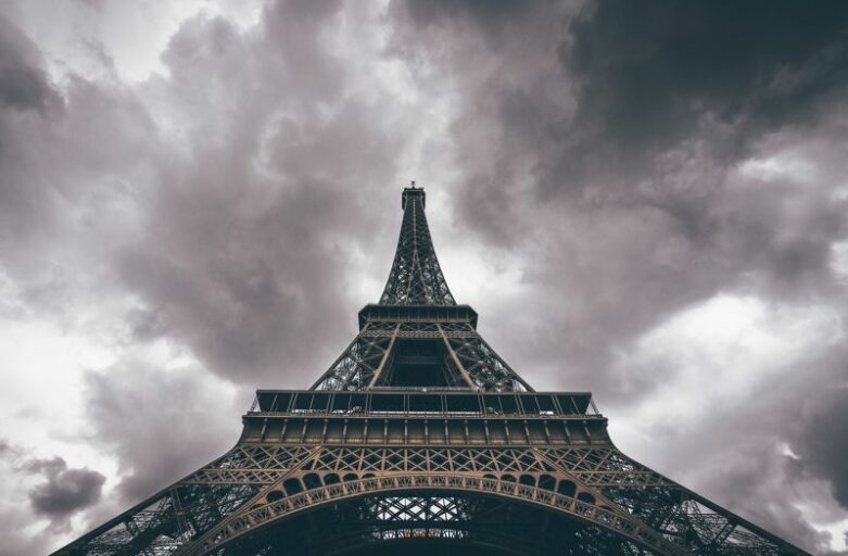 Klassenfahrt Paris Tickets Eiffelturm - auf dem Bild sehen wir den Eiffelturm in schwarz-weiß von unten mit seiner Spitze in einem bewölkten Himmel.